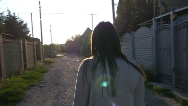 Al rallentatore, una ragazza con i capelli lunghi cammina lungo la strada tra le case al tramonto — Video Stock