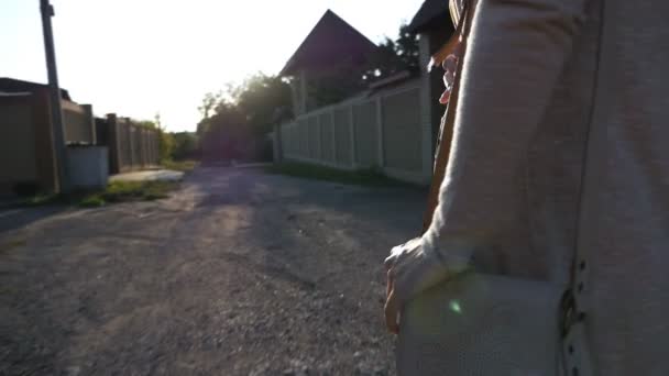 Стрельба сзади, вода сзади, девушка с длинными волосами идет по улице между домами на закате — стоковое видео