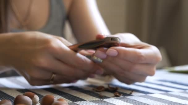 Primo piano delle mani di una ragazza che siede a un tavolo e pulisce una nocciola. Saporito, noci sane — Video Stock