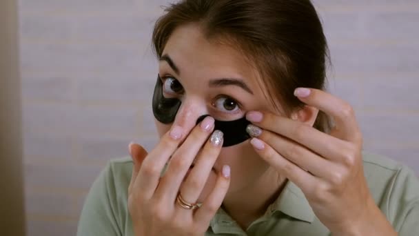 Het meisje gebruikt zwarte vlekken onder haar ogen, glimlachend, zittend tegenover de spiegel. Gezonde levensstijl, jeugd, gezicht — Stockvideo