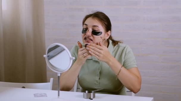 Ta dívka u zrcadla má na tváři kosmetické postupy. Ta holka dává korejský make-up do oblasti pod očima. To děvče si pohrává, škleby se, rozčiluje — Stock video