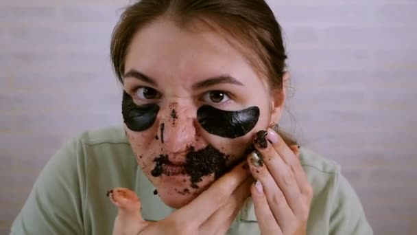Flickan nära spegeln utför kosmetiska ingrepp på hennes ansikte. Flickan sätter koreanska makeup på området under hennes ögon. Flickan lurar runt, grimasering, arg — Stockvideo