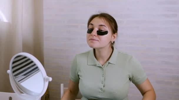 La ragazza vicino allo specchio esegue procedure cosmetiche sul suo viso. Cosmetici coreani ragazza, macchie nere sulla zona sotto gli occhi. Si pulisce il viso con un asciugamano — Video Stock