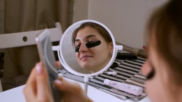 Ta dívka doma monitoruje kůži kolem očí, kosmetická péče, Korejská kosmetika, skvrny pod očima. Dívka používá telefon — Stock video