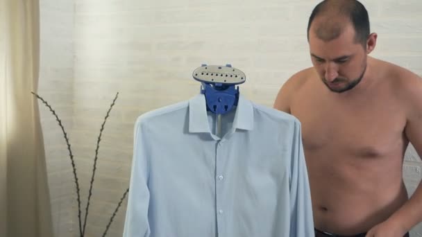 Процес пропарювання одягу. Лисий мужик одягає синю сорочку — стокове відео