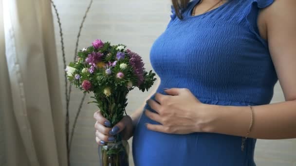 En ung gravid kvinna luktar en blomma, röra magen — Stockvideo
