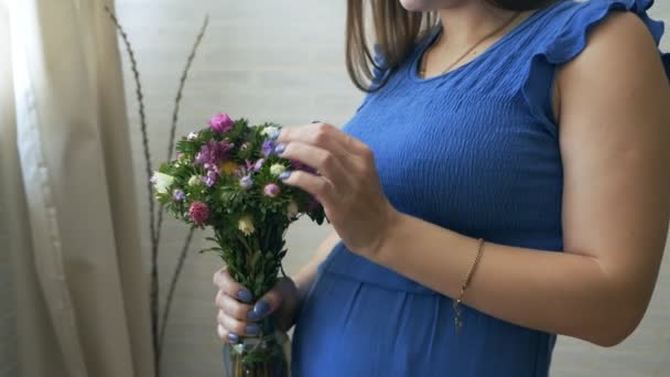 En ung gravid kvinna luktar en blomma, röra magen — Stockvideo