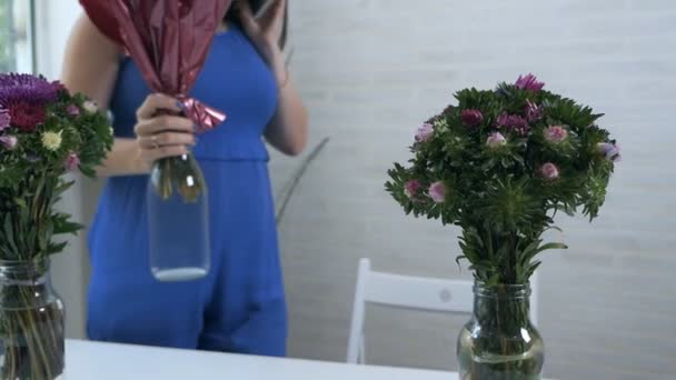 En ung flicka hemma sätter buketter av blommor i en vagn med vatten — Stockvideo