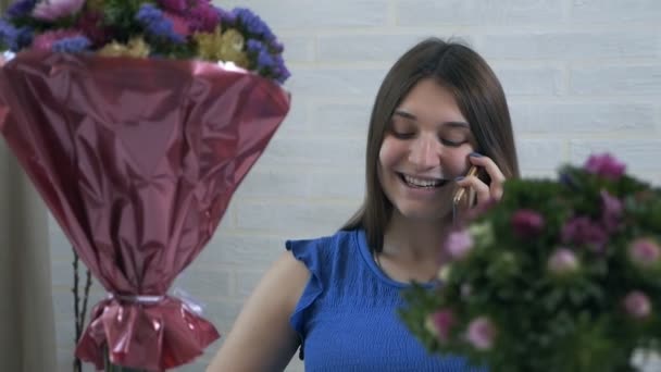 Ένα νεαρό κορίτσι στο σπίτι βάζει μπουκέτα λουλουδιών σε ένα κάρο με νερό και μιλά στο τηλέφωνο — Αρχείο Βίντεο