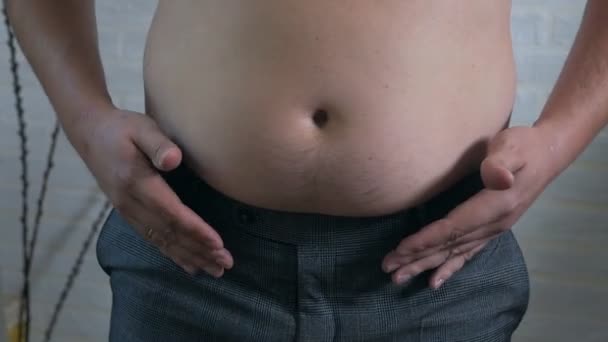 Close-up, estômago masculino, excesso de peso. Jovem com uma barriga gorda nua treme dobras de gordura em seu estômago, obesidade, saúde, barriga de cerveja — Vídeo de Stock