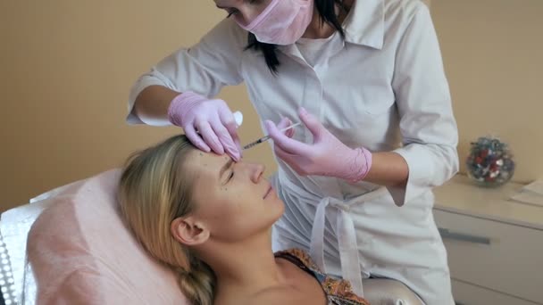 Clínica de belleza. Manos esteticistas con guantes haciendo inyecciones de envejecimiento facial en la piel femenina. La mujer recibe tratamientos faciales cosméticos. Inyecciones de colágeno Botox — Vídeos de Stock