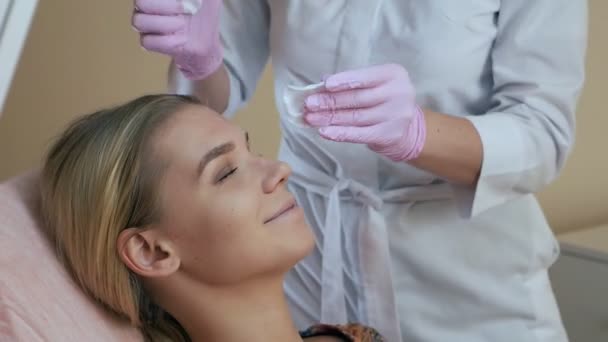 Kosmetikerin wischt dem Kunden das Gesicht mit einem Wattepad ab und bereitet sich auf den Eingriff vor — Stockvideo