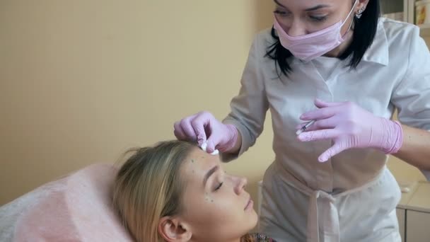 医師は、外科クリニックの部屋で顔のしわを取り除くために、眉間の額に中年の女性にフェイスリフトを注入します — ストック動画