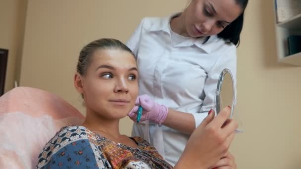Mooie vrouw bekijkt zichzelf in de spiegel na cosmetische ingrepen in de schoonheidssalon — Stockvideo