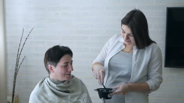 Вагітна стилістка перемішує фарбу для волосся в чорну миску. Підготовка фарби для волосся — стокове відео