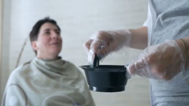 Stylist stirs hair dye in a black bowl. Hair dye preparation — Stock Video