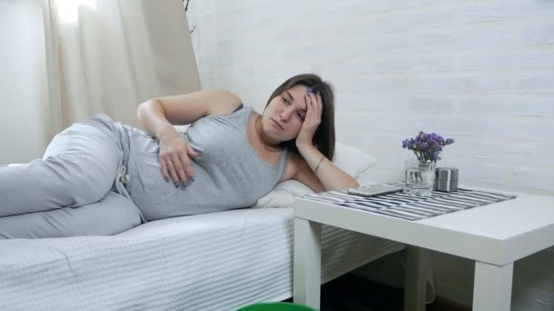 입덧. 젊은 임산부는 소파에 누워 양동이에 구토합니다. 임신 중독 — 비디오