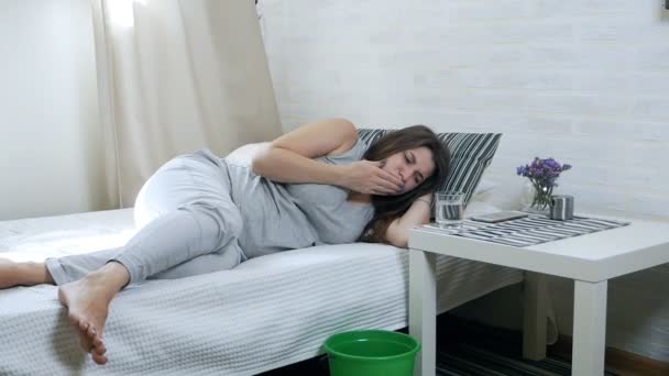 Утренняя тошнота. Молодая беременная женщина лежит на диване и блюет в ведро. Опьянение от беременности — стоковое видео