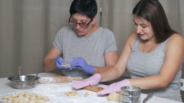 Uma menina grávida e sua mãe sentam-se a uma mesa na cozinha da casa e preparam bolinhos com carne picada para o almoço, rolam a massa com um rolo — Vídeo de Stock