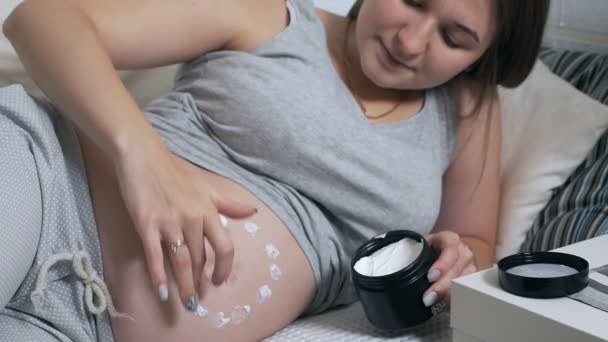 Glückliche Schwangere, die zu Hause auf der Couch liegt, cremt den Bauch ein — Stockvideo