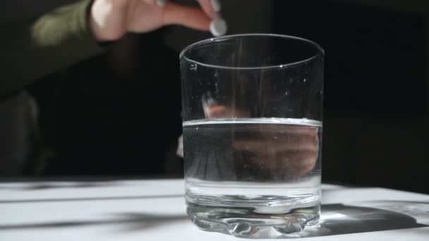 Een bruisende tablet tegen pijn valt in een glas en lost op. Aspirine tablet in een glas. Behandeling — Stockvideo