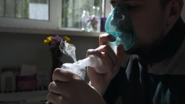 Junger Mann mit einer Maske aus einem Inhalator zu Hause. behandelt Entzündungen der Atemwege mittels Vernebler. Prävention von Asthma und Husten — Stockvideo