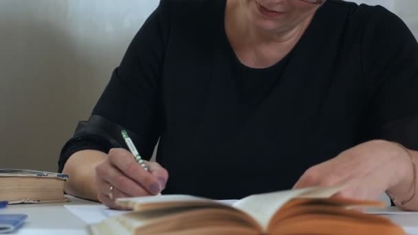 Uma mulher de óculos com um lápis na mão toma notas em papel, pensa e pondera, compõe um poema, um verso. Criatividade da poetisa — Vídeo de Stock