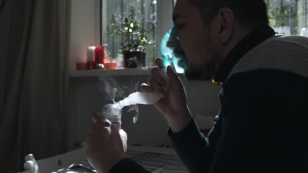 Junger Mann mit einer Maske aus einem Inhalator zu Hause. behandelt Entzündungen der Atemwege mittels Vernebler. Prävention von Asthma und Husten — Stockvideo