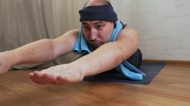 Ung skallig brutal man försöker göra yoga på golvet i sin lägenhet — Stockvideo