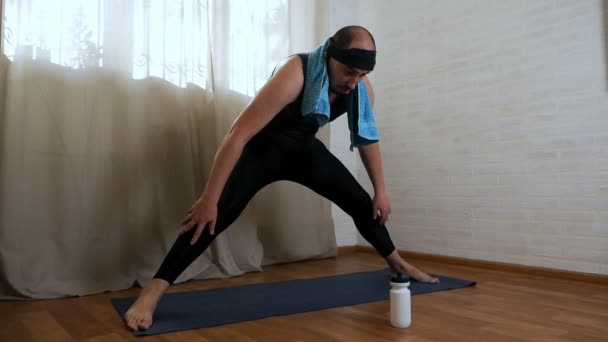 Hombre gordo divertido está tratando de hacer ejercicios de yoga en la alfombra. Yogui masculino brutal con ropa ajustada — Vídeo de stock