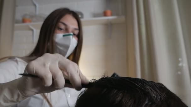 Una mujer joven con una máscara de medicina tiñe el pelo de sus madres en casa durante el brote del virus. Autocuidado en casa — Vídeo de stock