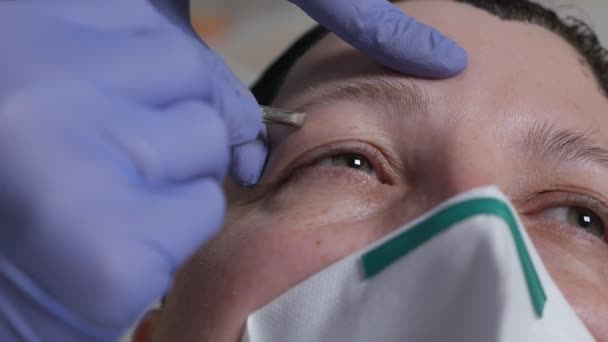 Cosmetische procedure voor wenkbrauwverzorging tijdens het virus. Een vrouw met een masker en handschoenen plukt pincet met een wenkbrauw aan een gemaskerde cliënt tijdens het virus. — Stockvideo