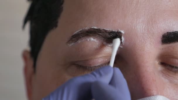 Un maquillador con guantes corrige, moldea y colorea las cejas del cliente con una máscara protectora en casa durante el virus. Cuidado personal, concepto de cosmetología en el hogar — Vídeo de stock