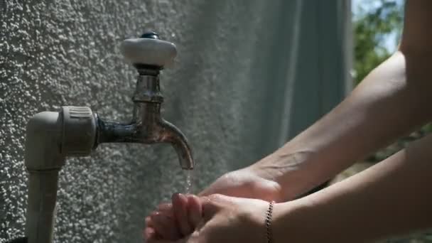 Водопроводный кран в общественном месте. Молодая женщина моет руки в городском фонтане — стоковое видео