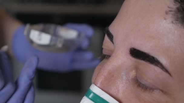 En ung kvinna i handske korrigerar, formar och färgar sin mors ögonbryn i en skyddande mask hemma under viruset. Personlig hygien, begreppet kosmetologi i hemmet — Stockvideo