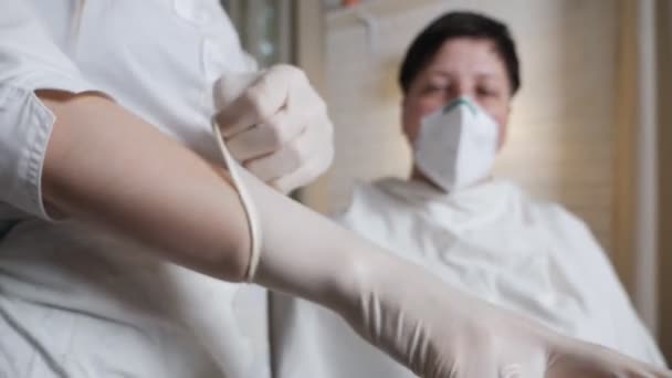 Молодая девушка в медицинской маске надевает перчатки, чтобы покрасить волосы матери дома во время изоляции — стоковое видео