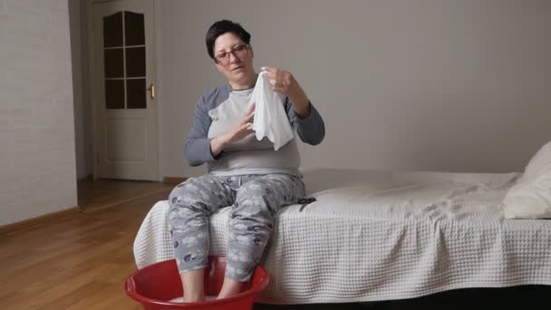 Egy otthon öregedő nő hámozást fog végezni, a kezében tartja, és speciális zoknikat vizsgál pedikűrözéshez. SPA pedikűr, láb- és körömápolás — Stock videók
