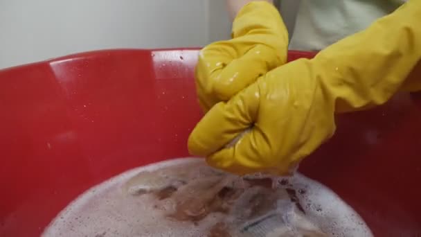 Een vrouw wast kleren, een handdoek in een wasbak met een wasmiddel in handschoenen. Hoe de verf eraf te wassen. Dingen uit het water spinnen — Stockvideo