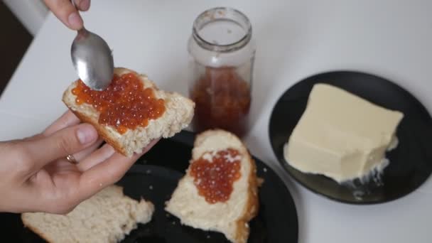 Kvinnlig hand lägger röd kaviar på bröd med en sked. smörgåsar med smör och kaviar. Hemlagad mat — Stockvideo