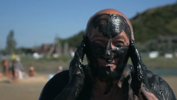 Un uomo anziano si spalma il viso di fango medicinale nero sul mare con acqua salata. Fango nero e argilla sono utili per le persone con problemi di salute e pelle. Rilassati in un resort termale — Video Stock