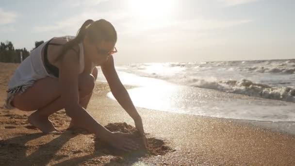 Attraente giovane donna costruzione castello di sabbia sulla spiaggia al tramonto — Video Stock