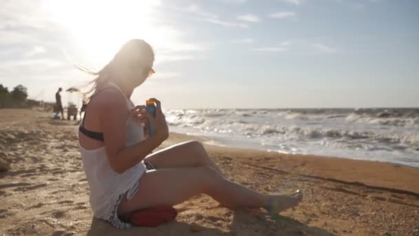 Mujer atractiva con piel sana, con protector solar en el hombro, mano mientras está sentada en la playa cerca del mar — Vídeos de Stock