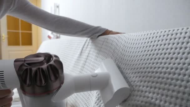 A nők kezei egy modern vezeték nélküli porszívóval tisztítják a kanapét egy speciális fúvókával, közelről. Tisztítási koncepció vezeték nélküli porszívóval — Stock videók