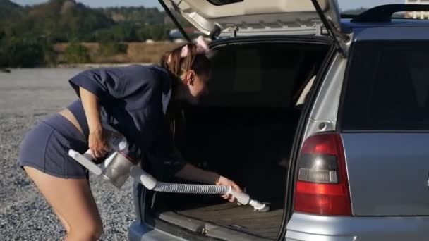 Женщина пылесосит багажник автомобиля с пылесосом удаляя грязь и пыль из багажника автомобиля на открытом воздухе на закате — стоковое видео