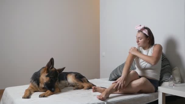 Donna che si prende cura della pelle. Donna sdraiata sul letto con cane da compagnia che applica lozione per le mani — Video Stock