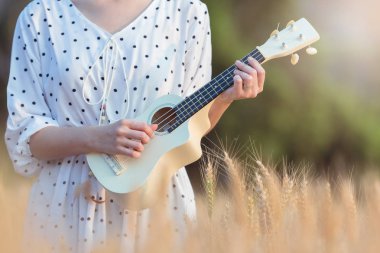 Ukulele oynama ve gün batımı zamanında yaz aylarında arpa sahasında rahatlatıcı güzel Asyalı kadın