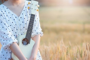 Ukulele oynama ve gün batımı zamanında yaz aylarında arpa sahasında rahatlatıcı güzel Asyalı kadın