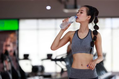 Fitness salonundaki antrenmandan sonra kulaklık takan kadın su içiyor..