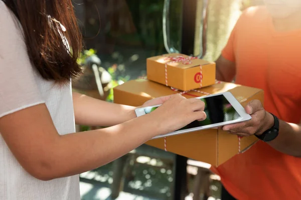 Customer sign signature in digital tablet after receiving parcel from delivery courier at home.