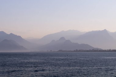 Mavi bir sis ve deniz üzerinde gün batımı dağlar